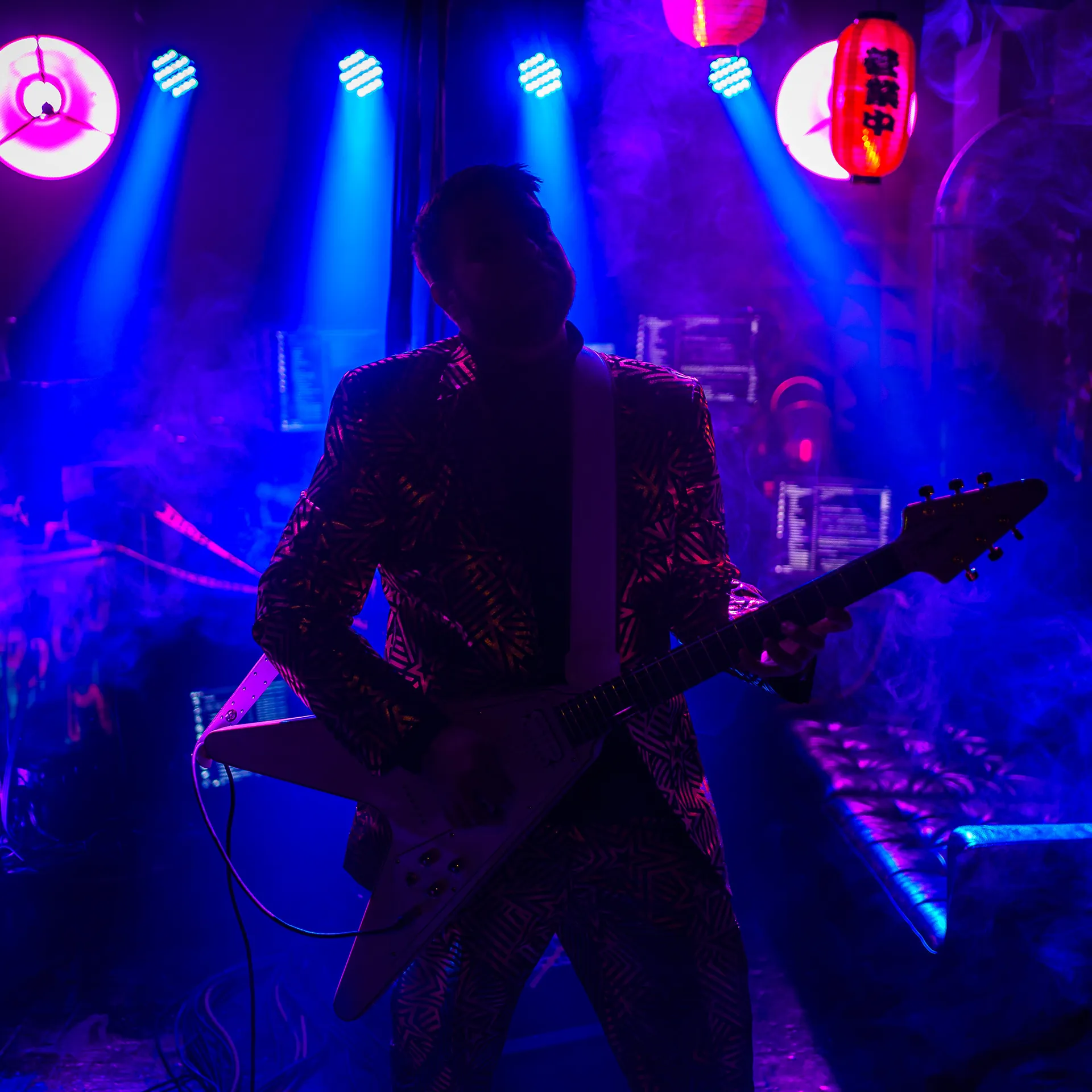 Silueta gitaristu King of Synthos v modro-fialových svetlách